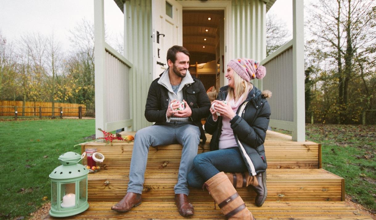 A couple sitting on the steps of a shepherd's hut at Snug Huts in East Yorkshire