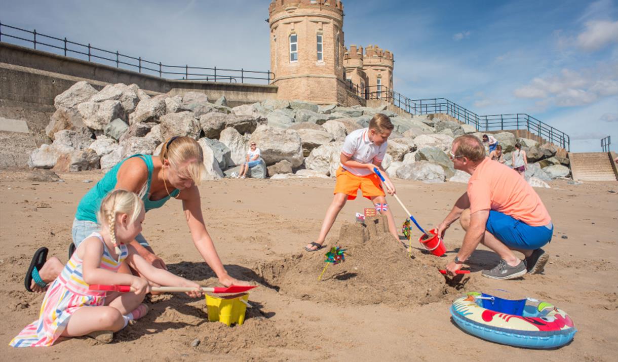 A family making sandcastles on the beach in front of Pier Towers at Withernsea, in East Yorkshire.