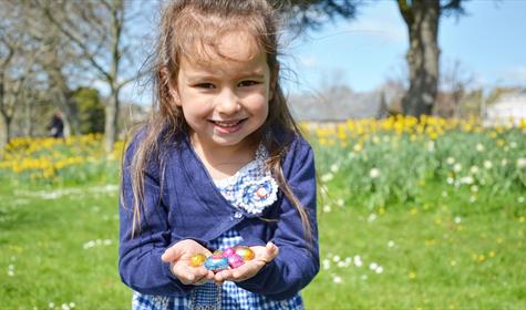 “Young girl holding chocolate eggs after an Easter egg hunt at a park on the English Riviera