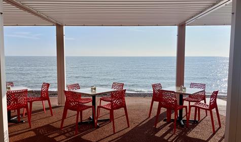 View of tables and chairs on the promenade looking out over a sparkling sea with blue sky above
