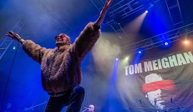 An Evening with Tom Meighan – The Original Voice of Kasabian Palace Theatre Paignton picture of Tom Meighan on stage in a fake fur bomber jacket 