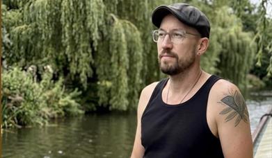 Robbie in a vest top on a canal boat with trees and water in the background