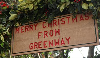 Wooden sign that says 'Merry Christmas from Greenway' surrounded by green leaves