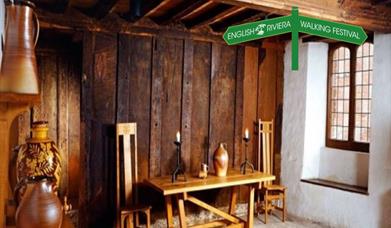 The interior of Kirkham House in Paignton, with wooden furniture and ceramic storage jars, wood panelled walls.