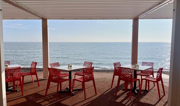 View of tables and chairs on the promenade looking out over a sparkling sea with blue sky above