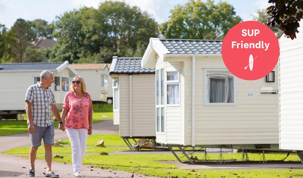 A man and a woman walk hand in hand against a backdrop of static caravans, at Beverley Holiday Park in Paignton