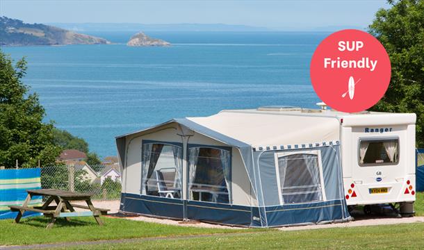 A caravan with awning against a wide sea view, at Beverley Holidays in Paignton