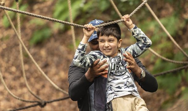 A child smiling and having fun on playing on ropes guided by their parent.