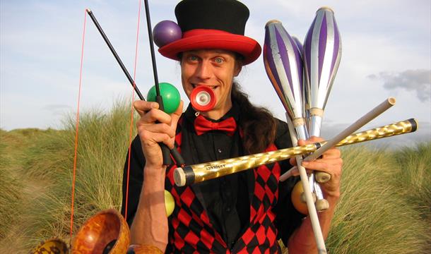 A circus performer holding lots of equipment in a comedic way including juggling batons and diablos.