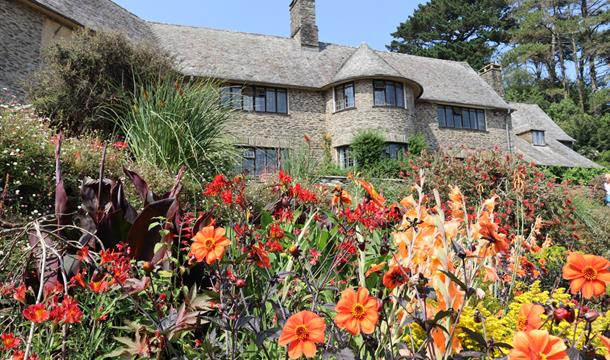 Red, orange and yellow flowers in the border with the stone house in the background.