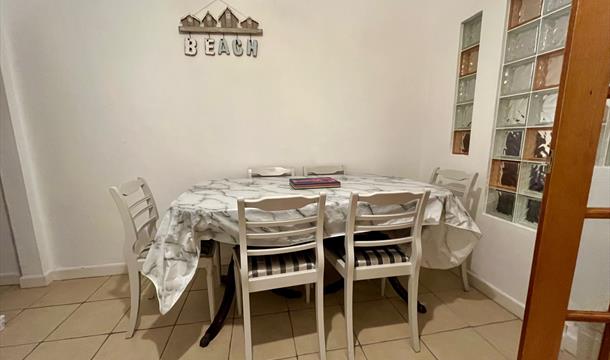 Dining area with extendable table and 6 chairs. The floor is tiled and there is a Beach artwork on the wall. There are glass tiles in the wall leading