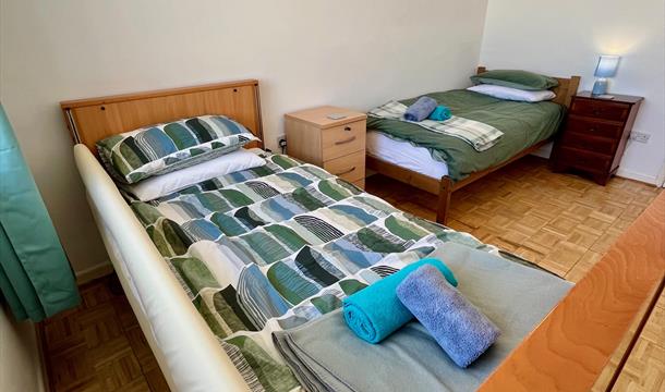 Rear bedroom with profile bed and single bed. There re bedside drawers and a bedside lamp. There is a print  of a seal on the wall.