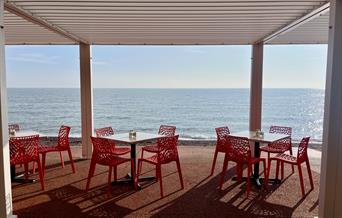 View of tables and chairs on the promenade looking out over a sparkling sea with blue sky above