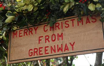 Wooden sign that says 'Merry Christmas from Greenway' surrounded by green leaves