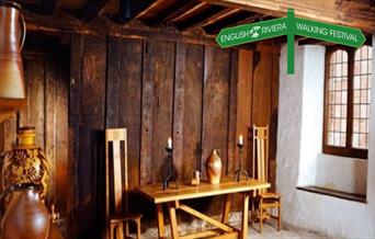 The interior of Kirkham House in Paignton, with wooden furniture and ceramic storage jars, wood panelled walls.