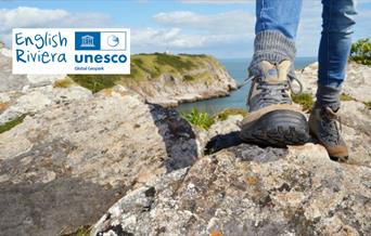 Closeup of a hiker's feet in walking boots, on rocks on the South West Coast Path. English Riviera UNESCO Global Geopark.