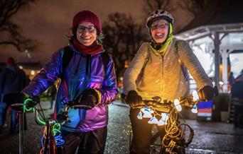 Two women with glowed up bikes and bright clothing on a dark night