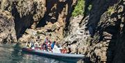 Torquay Watersports coastal wildlife boat tour - a boat in the shallows of turqoise waters below interesting rock formations in the cliffs beyond.