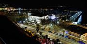 A view of the whole theatre from rock walk steps with the marina in the background. the venue is lit white at night time.