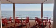 View of tables and chairs on the promenade looking out over a sparkling sea with blue sky above
