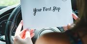 Woman in car holding envelope that read 'Your First Stop'