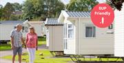A man and a woman walk hand in hand against a backdrop of static caravans, at Beverley Holiday Park in Paignton