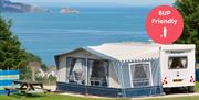 A caravan with awning against a wide sea view, at Beverley Holidays in Paignton