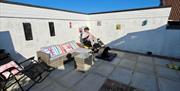 Back garden, with patio furniture and sun loungers. Wheelchair access through side gate from driveway. A person is in a wheelchair with a black Giant