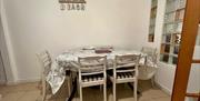 Dining area with extendable table and 6 chairs. The floor is tiled and there is a Beach artwork on the wall. There are glass tiles in the wall leading