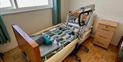 Bedroom with Profile bed and mobile electric hoist. The floor is wooden. There is a lockable chest of drawers. A picture of a seal is on the wall.