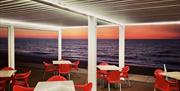 Outside tables and chairs and view out to sea with orange glow on the horizon as the sun rises