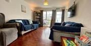 Lounge with electric Rise and recline chair, sofas, coffee table and TV. There is a wooden floor with a painting on the wall and a bookcase with lots