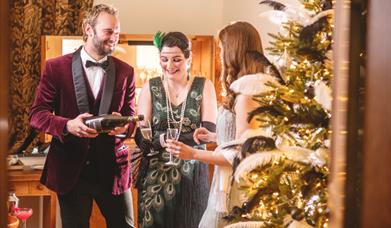 Three people dressed in vintage 1920s clothing drink champagne by a gold and black Christmas tree