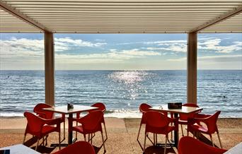 View of tables and chairs on the promenade looking out over a sparling sea with blue sky above