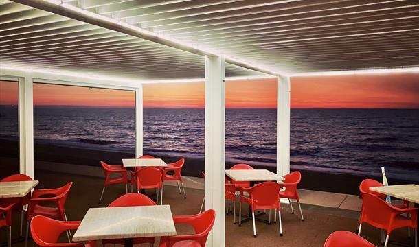 Outside tables and chairs and view out to sea with orange glow on the horizon as the sun rises