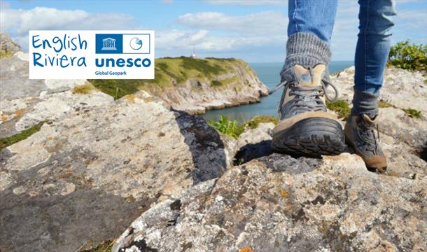 Closeup of a hiker's feet in walking boots, on rocks on the South West Coast Path. English Riviera UNESCO Global Geopark.