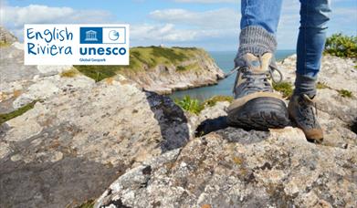 Closeup of a hiker's feet in walking boots, on rocks on the South West Coast Path. English Riviera UNESCO Global Geopark.