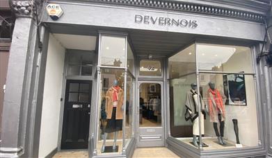 Outside Devernois in Blackheath. A silver shop front with three mannequins in the window wearing clothing items.