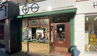 Outside For Eyes Opticians in Greenwich. A small and charming shop with a green and white design and a front window filled with glasses.