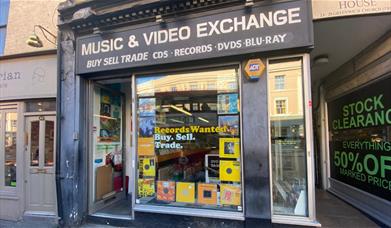 Outside Music & Video Exchange in Greenwich. A black and white shopfront with a huge selection of items inside.