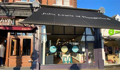 Outside John Lewis of Hungerford in Blackheath. A black and white shop front with a large window showing off a range of kitchens inside.