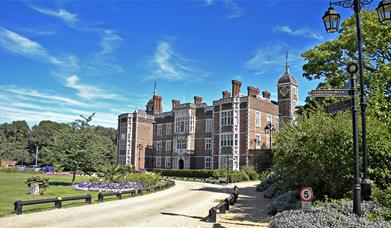 The front of Charlton House on a sunny summer's day surrounded by lush green grass and flowers.