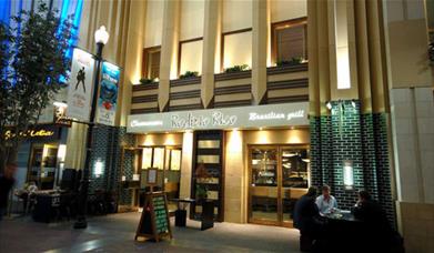 Outside Rodizio Rico at the 02, showing a stunning beige, green and white building with outdoor and indoor seating.