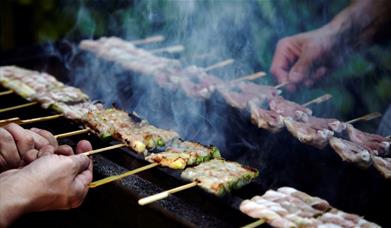 Small wooden sticks of meat, fish and cheese being grilled over open flame at Sticks'n'Sushi.