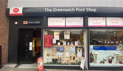 Outside Greenwich Post Office. A black, red and white shopfront with a window showing envelopes and other stationary.