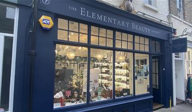 Outside The Elementary Beauty Company in Greenwich. An elegant navy blue shop front with windows that show a range of beauty products.