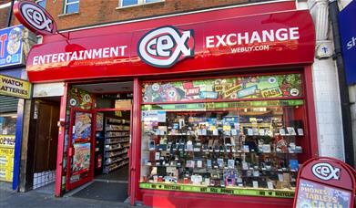 Outside CeX in Eltham. Showing a red and white shop with a selection of electronics presented through the window.