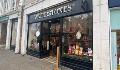 Outside Waterstones in Greenwich, showing a black shop front with a range of books through the window.