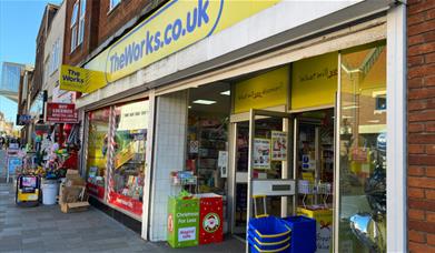 Outside The Works Eltham. showing a blue and yellow themed shop front.