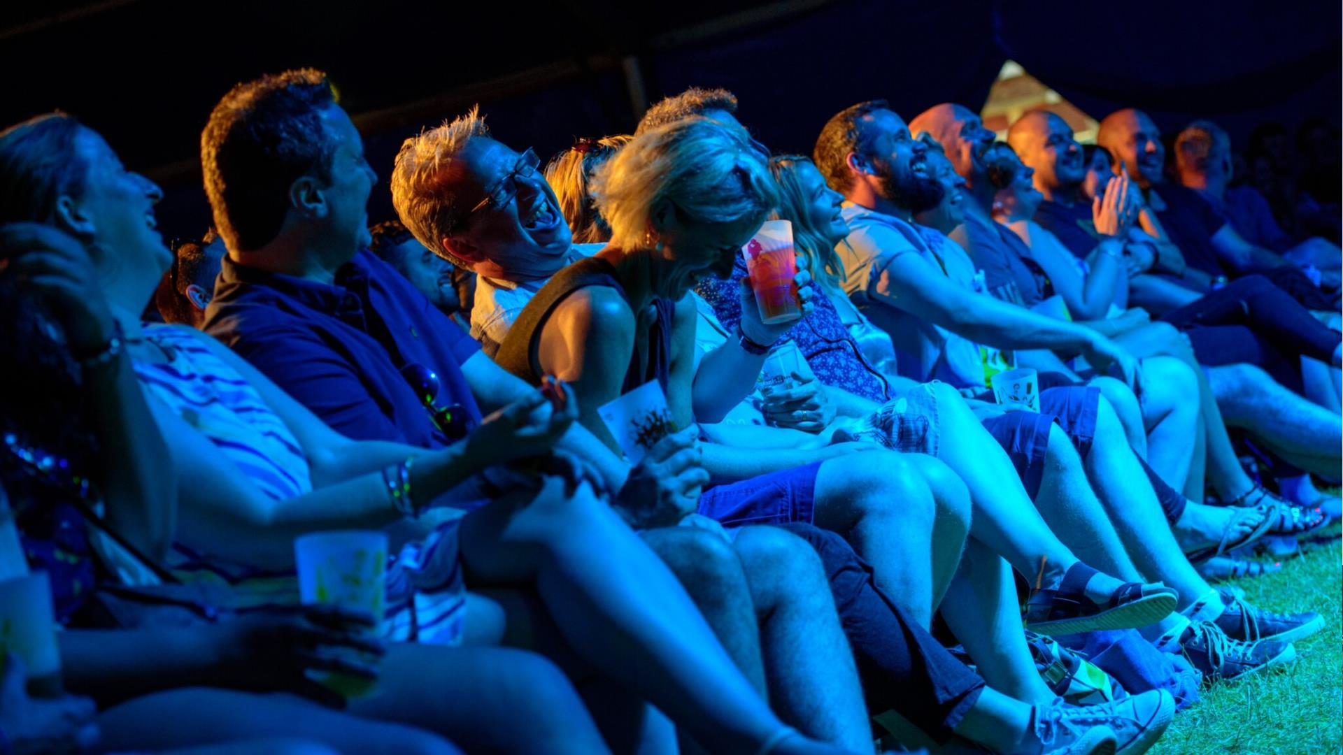 People in the front row of an event in Greenwich laughing at the act on stage.